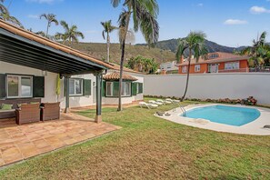 A residential property with a swimming pool, patio furniture, and a view of a hilly landscape.