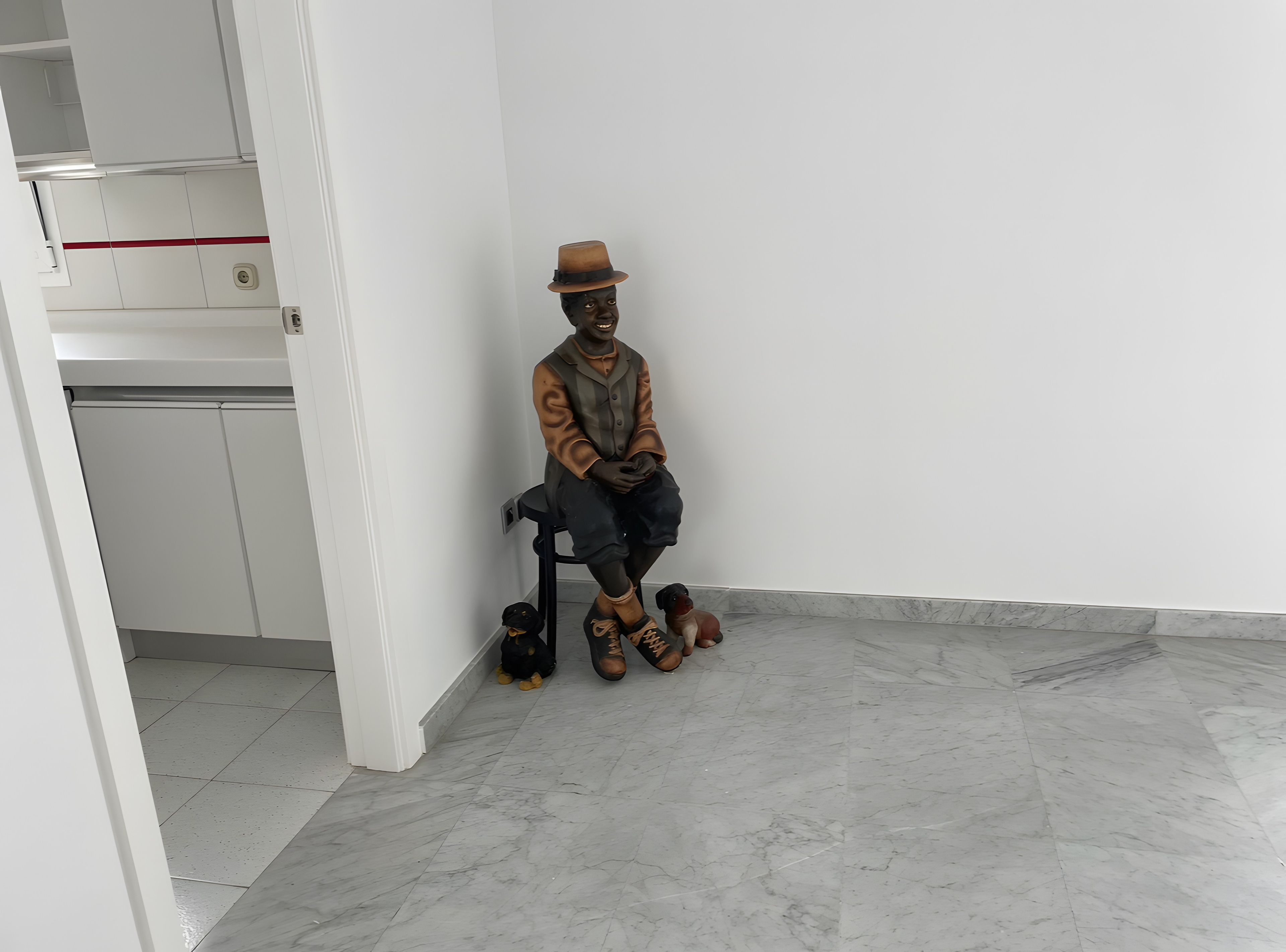 A statue of a man in a hat sitting on a chair in a room with a tiled floor and white walls.