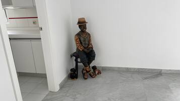 A statue of a man in a hat sitting on a chair in a room with a tiled floor and white walls.