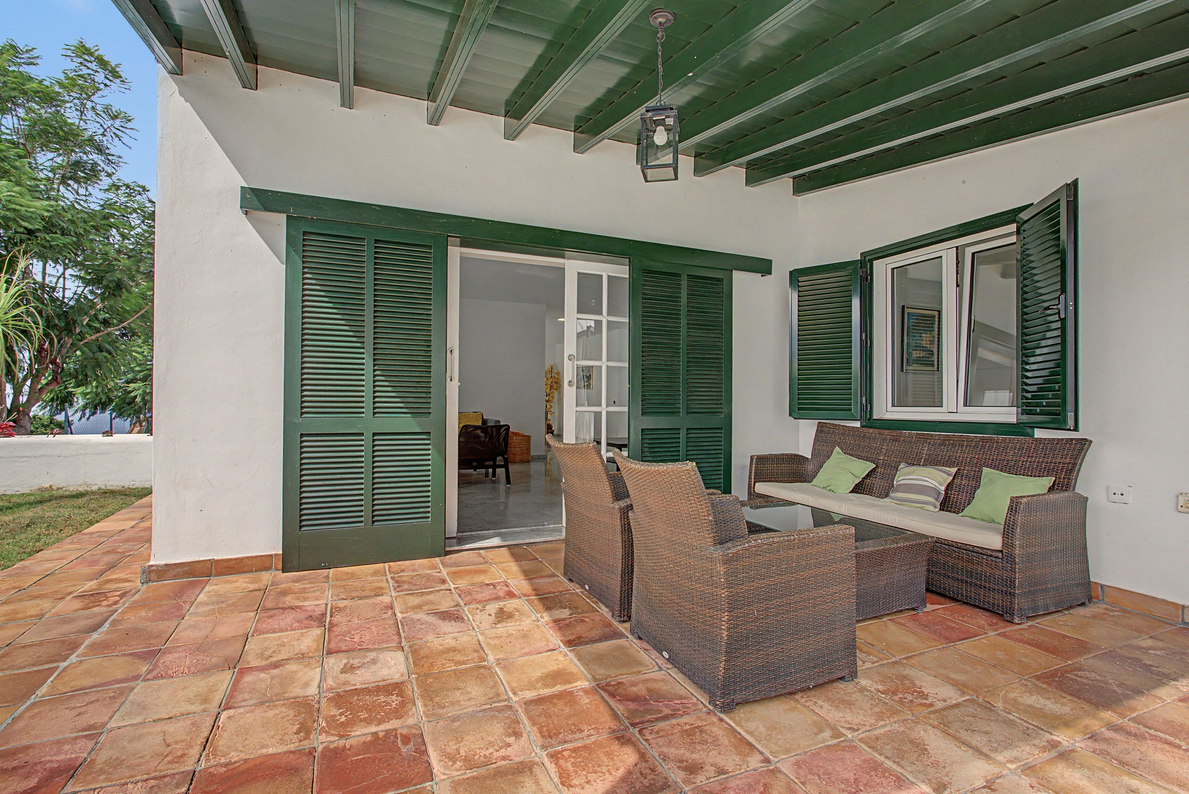 An outdoor patio area with a wicker sofa, a table, and green shutters on the windows.