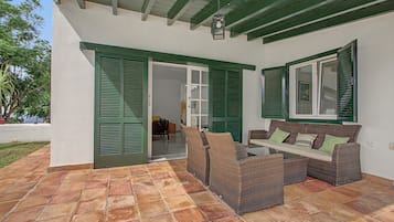 An outdoor patio area with a wicker sofa, a table, and green shutters on the windows.