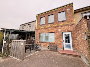 A two-story brick building with a wooden exterior, a bench, and a bicycle parked outside. - Fischerstuuv - 50-square-meter apartment for 2 in downtown Husum (Husum)