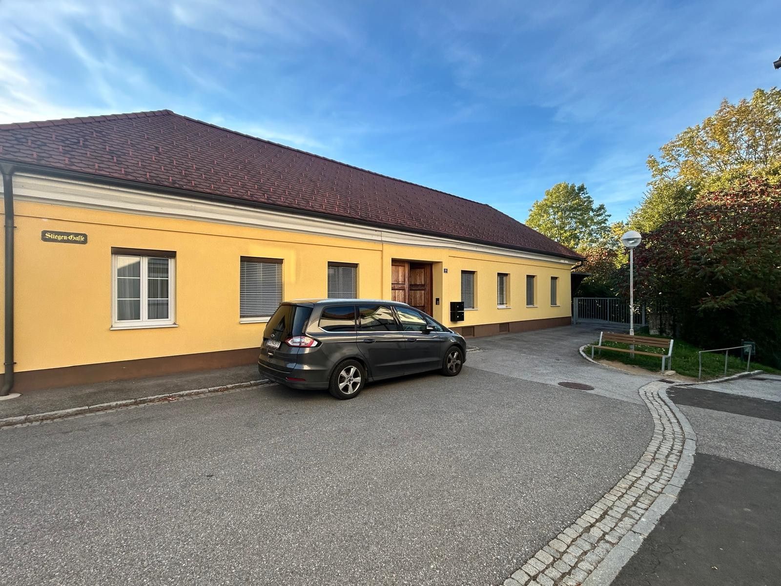 Ein Gebäude mit gelber Fassade, ein geparktes Auto und ein klarer Himmel.