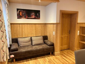 A cozy room with a wooden panel wall, a brown sofa with patterned cushions, a wooden door, and a framed picture above the sofa.