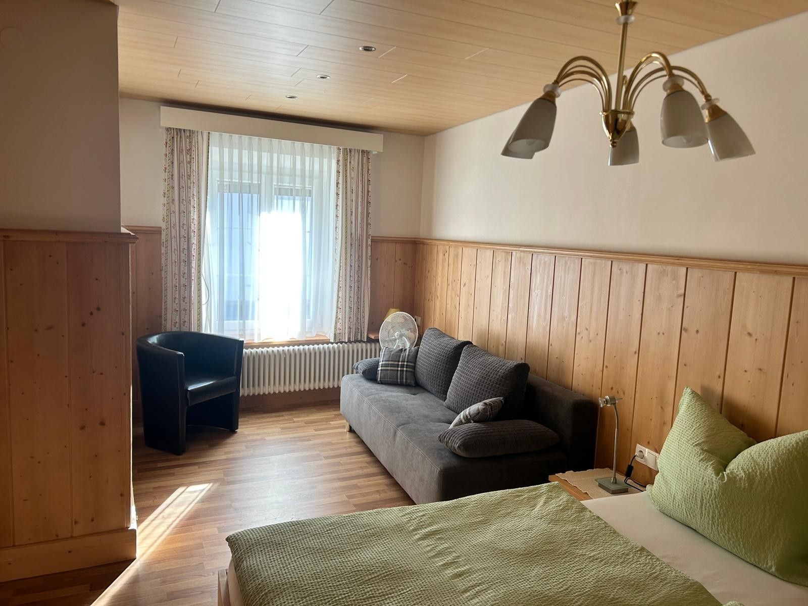 Una habitación con cama, sofá, silla, radiador y ventana con cortinas.