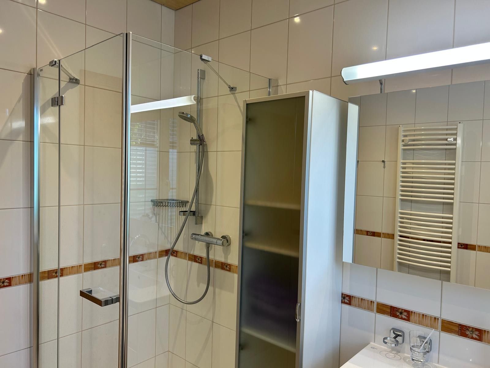 Ein modernes Badezimmer mit einer Duschkabine aus Glas, einem Waschtisch inklusive Spiegel und einem Handtuchhalter.
