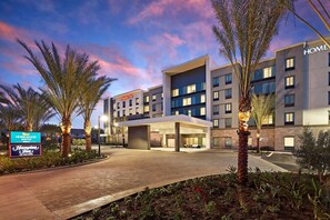 Un hôtel moderne doté d’une entrée couverte, de palmiers et d’une enseigne indiquant « Homewood Suites by Hilton ».