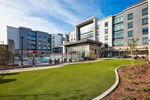 Un hotel moderno con piscina, mobiliario exterior y un césped bien cuidado.