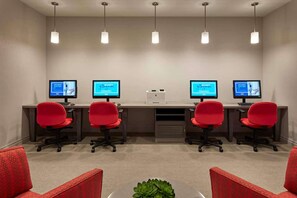 Une salle de conférence équipée de quatre bureaux, chacun doté d’un écran d’ordinateur affichant un fond bleu avec du texte, d’une imprimante et de chaises rouges.