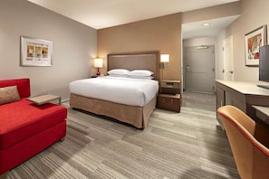 Una habitación de hotel con cama, sofá rojo, escritorio y televisor.
