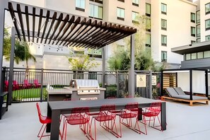 Un patio al aire libre con una parrilla, zona de estar y una pérgola.
