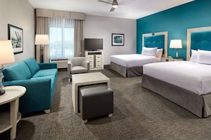 Ein Hotelzimmer mit Bett, Sofa, Schreibtisch, Stuhl, Fernseher und einem Fenster mit Vorhängen.