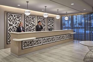 Ein Hotelrezeptionstresen mit modernem Design, inklusive einem gemusterten Trennelement und Pendelleuchten.