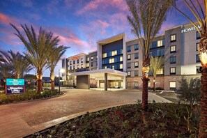 A modern hotel with a covered entrance, multiple floors, and a landscaped area with palm trees. - King Studio w/ Kitchen near the Airport + Shuttle (Long Beach)