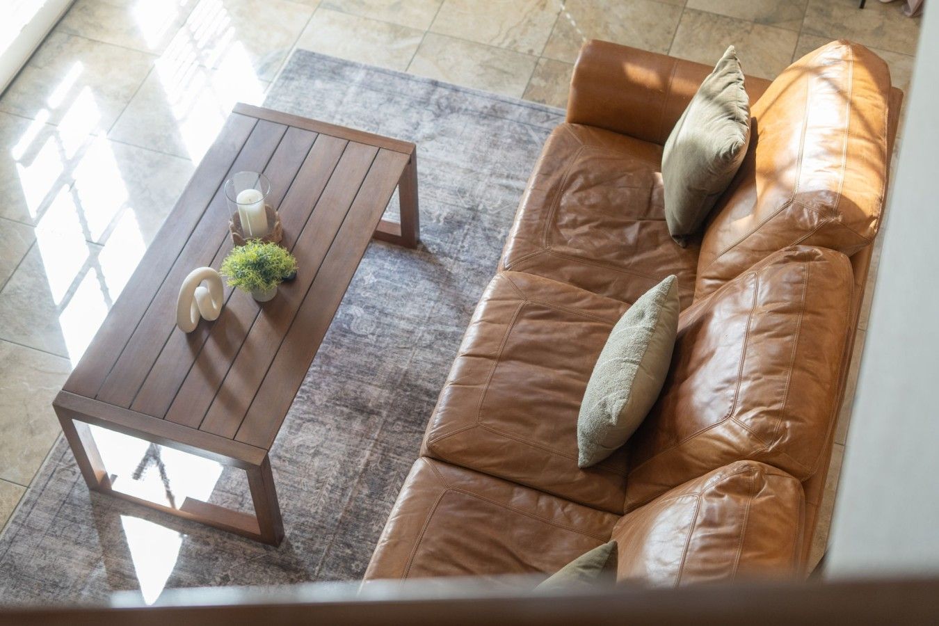 A brown leather sofa with cushions and a wooden coffee table with a small plant and candle.