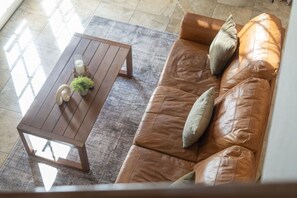 Un sofá de cuero marrón con cojines y una mesa de centro de madera con una planta pequeña y una vela.