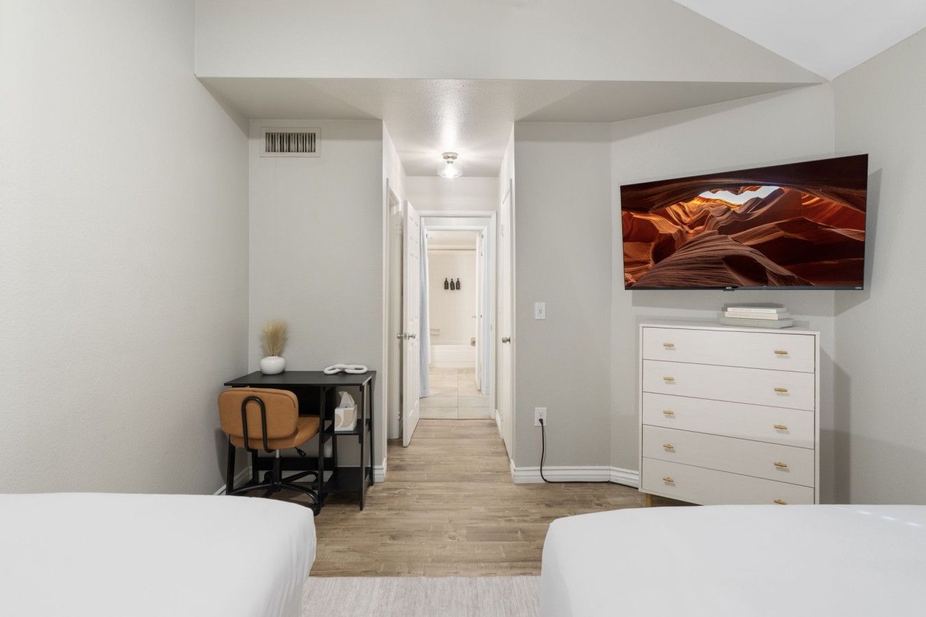 A hotel room with a bed, a desk with a chair, a dresser, and a TV mounted on the wall.