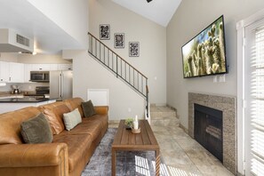 Una sala de estar moderna con un sofá de cuero, una chimenea, una escalera y una cocina al fondo.