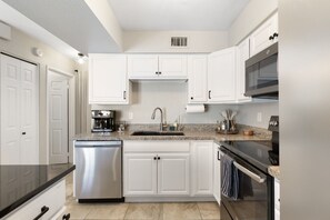Una cocina con gabinetes blancos, lavavajillas de acero inoxidable, encimera de granito, microondas empotrado y horno de acero inoxidable.