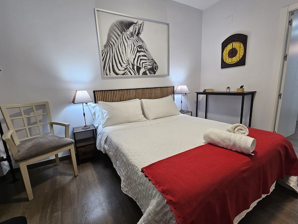 Ein Hotelzimmer mit Bett, Sessel, Nachttisch, Tisch und Bildern an den Wänden.