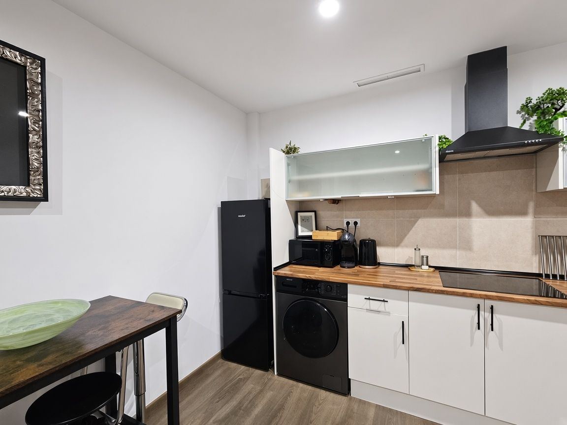 Een kleine keuken met een wasmachine, een magnetron en een koffiezetapparaat op het aanrecht.