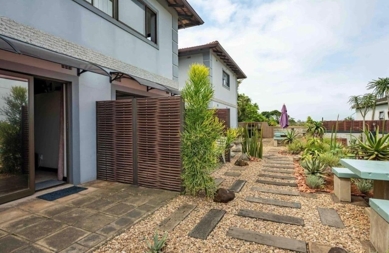 A modern house with a patio area featuring a stone pathway, a wooden fence, and various plants.