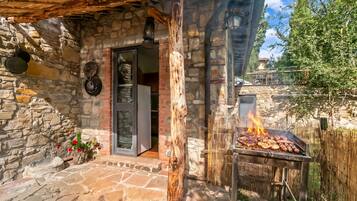 A stone building with a wooden door, a grill outside, and a stone wall.