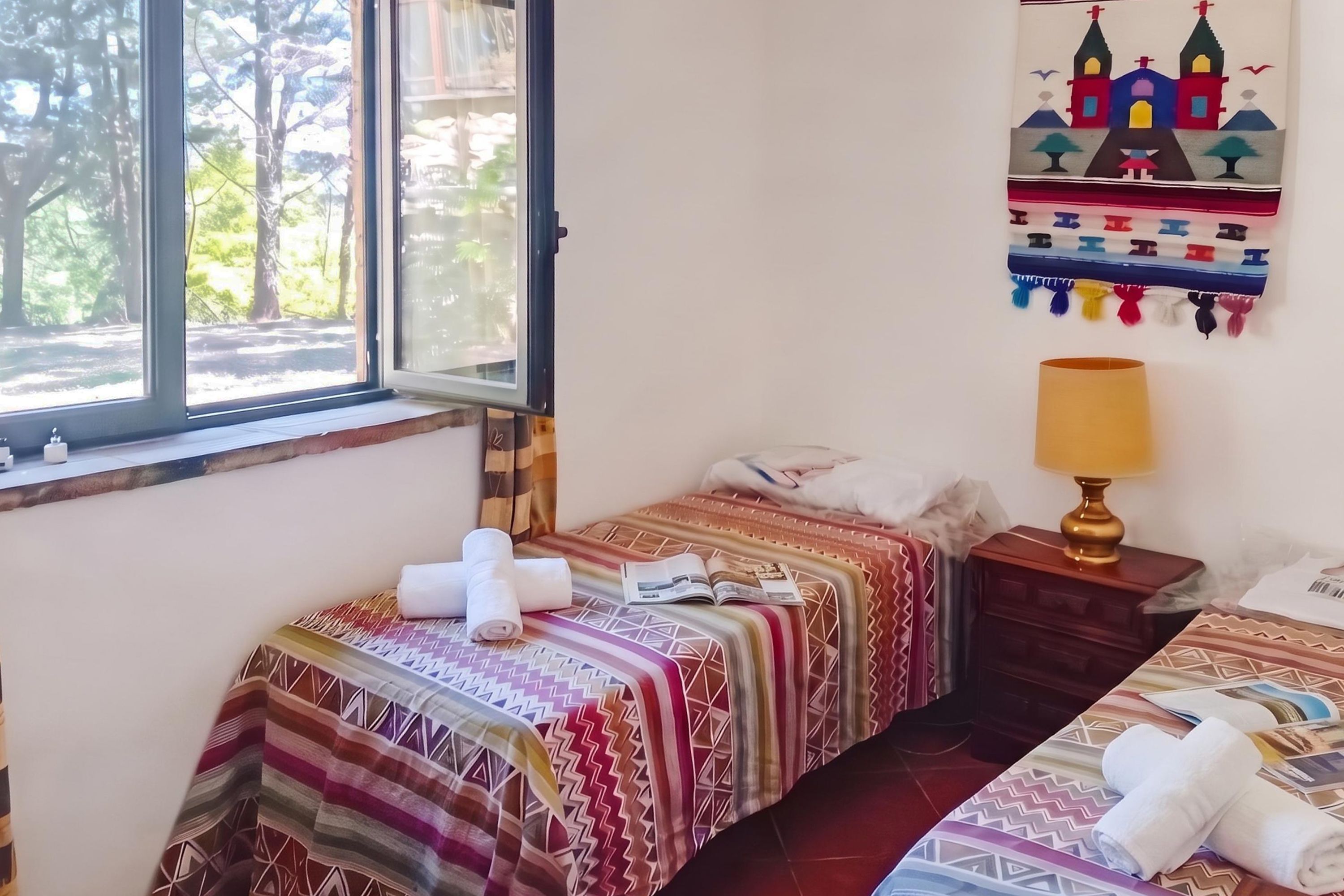 Una habitación con dos camas, una ventana con vista a árboles, una obra de arte en la pared y una lámpara de noche.