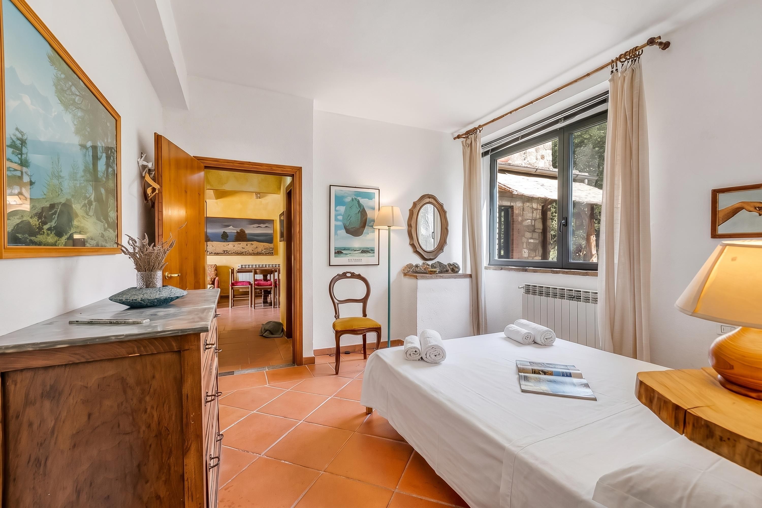 A hotel room with a bed, a desk, a chair, a window with curtains, and artwork on the walls.