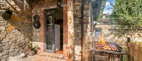 Un edificio de piedra con puerta de madera, una parrilla en el exterior y un muro de piedra.