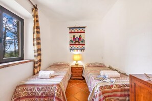 A small, cozy room with two beds, a window with a view of trees, and a hanging tapestry.