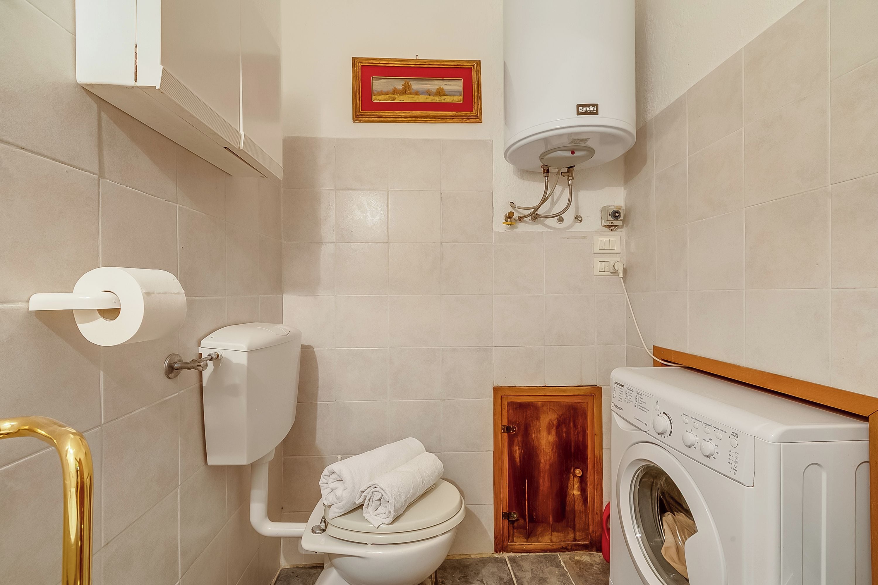 Ein Badezimmer mit Toilette, Waschmaschine, Handtuchhalter und einem gerahmten Bild an der Wand.