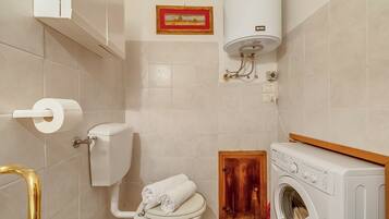 Ein Badezimmer mit Toilette, Waschmaschine, Handtuchhalter und einem gerahmten Bild an der Wand.