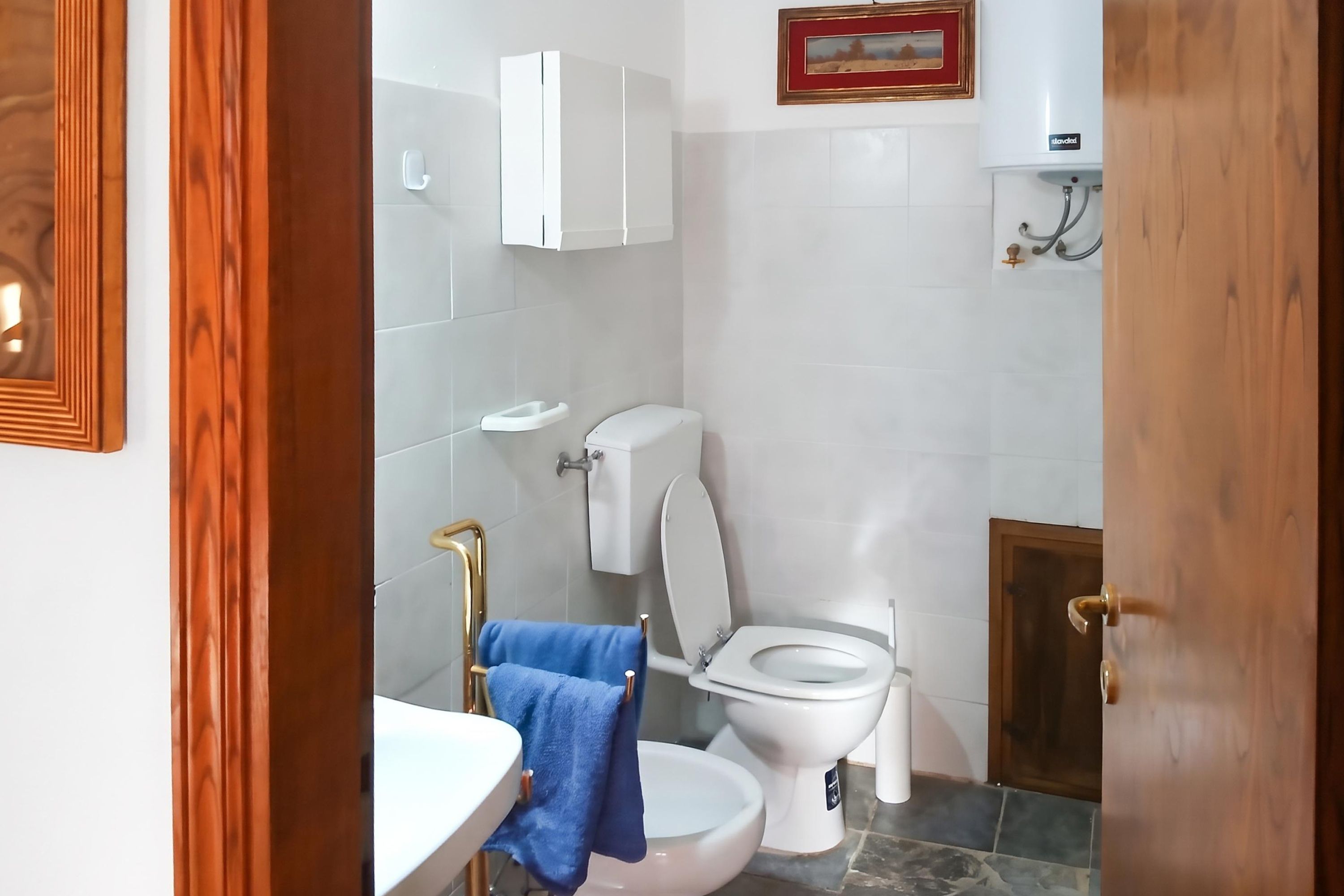 Un baño con inodoro, lavamanos y perchero para toallas.