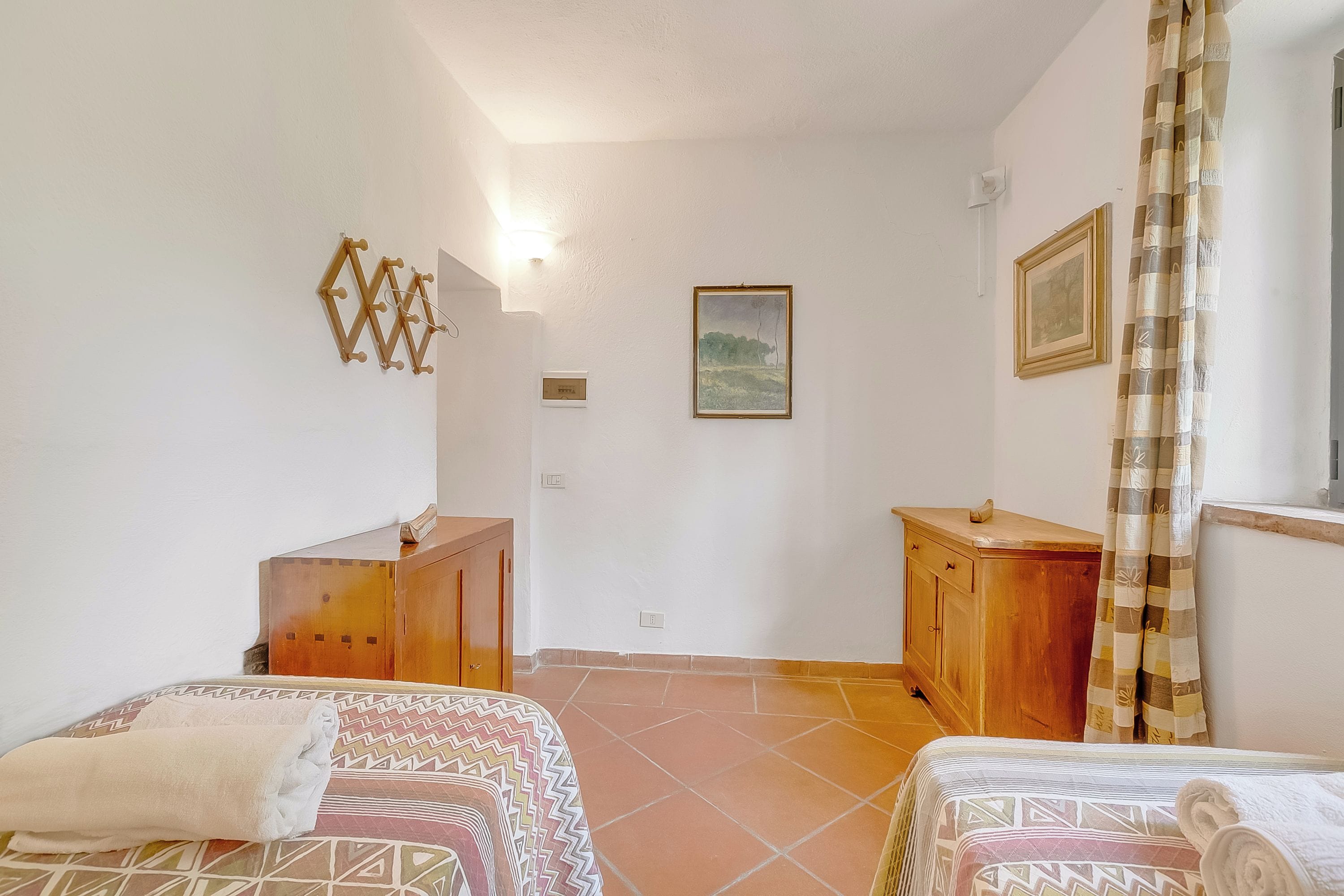 Un dormitorio con dos camas, un aparador de madera, un cuadro en la pared y una ventana con cortinas.