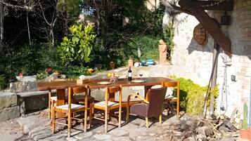 An outdoor dining area with a stone table and chairs, surrounded by greenery and a stone wall.