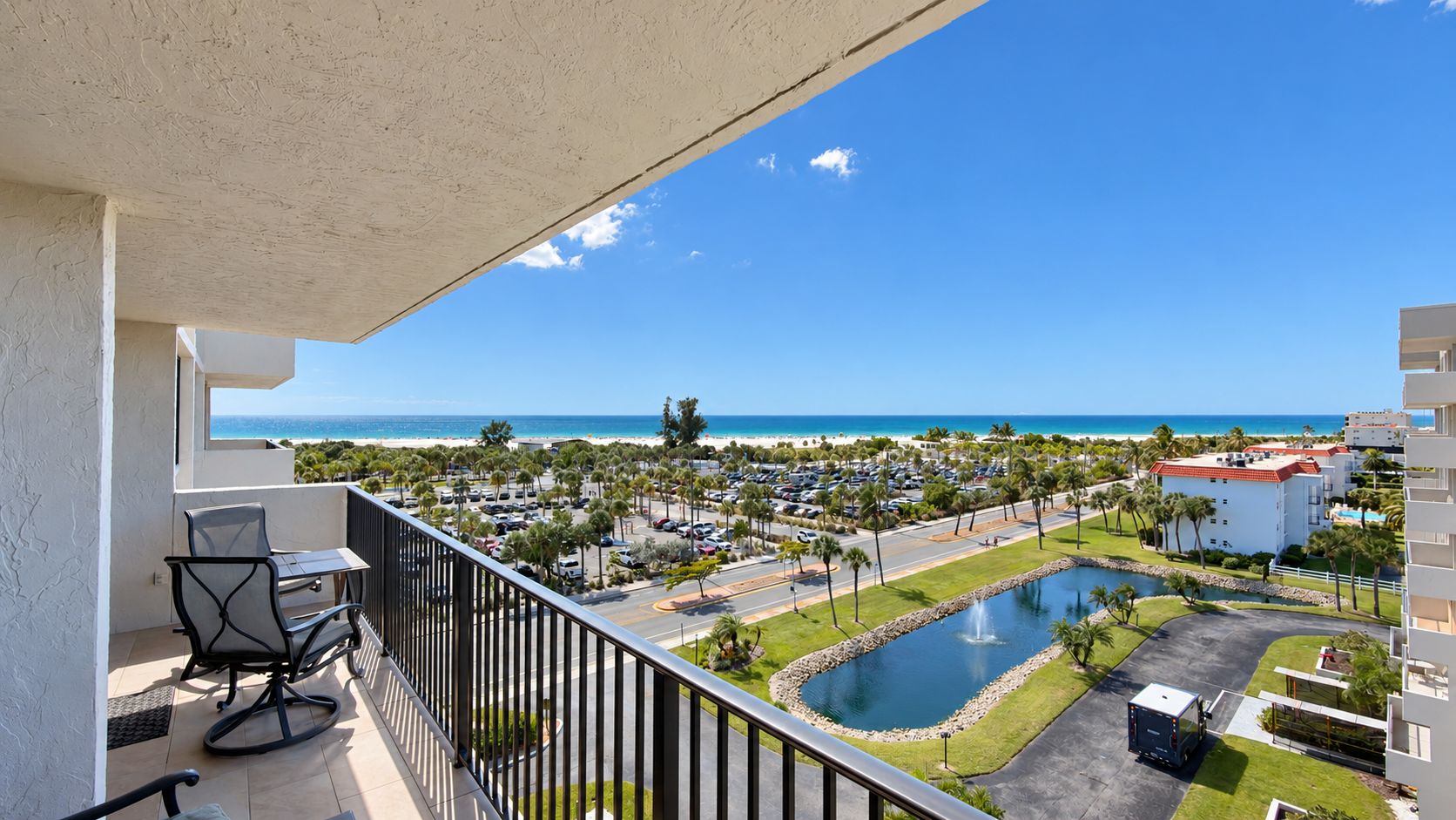 A balcony with a view of a beach, a parking lot, and a pool area.