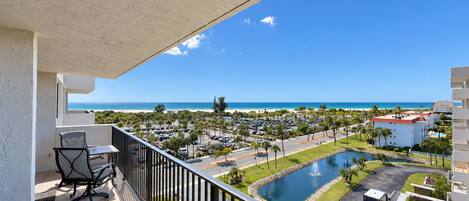 A balcony with a view of a beach, a parking lot, and a pool area.