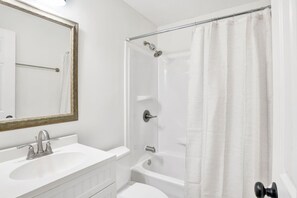 A bathroom with a white sink, a mirror with a gold frame, a shower with a glass door, and a white shower curtain. - Southern Comfort (Mobile)