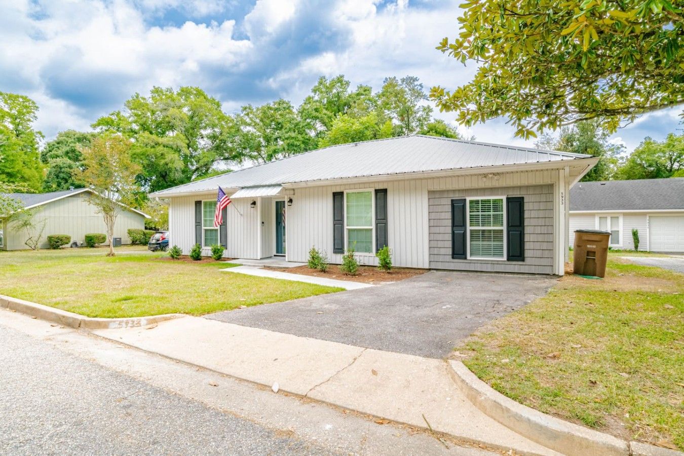 A single-story residential building with a front porch, a flag, and a well-maintained lawn.