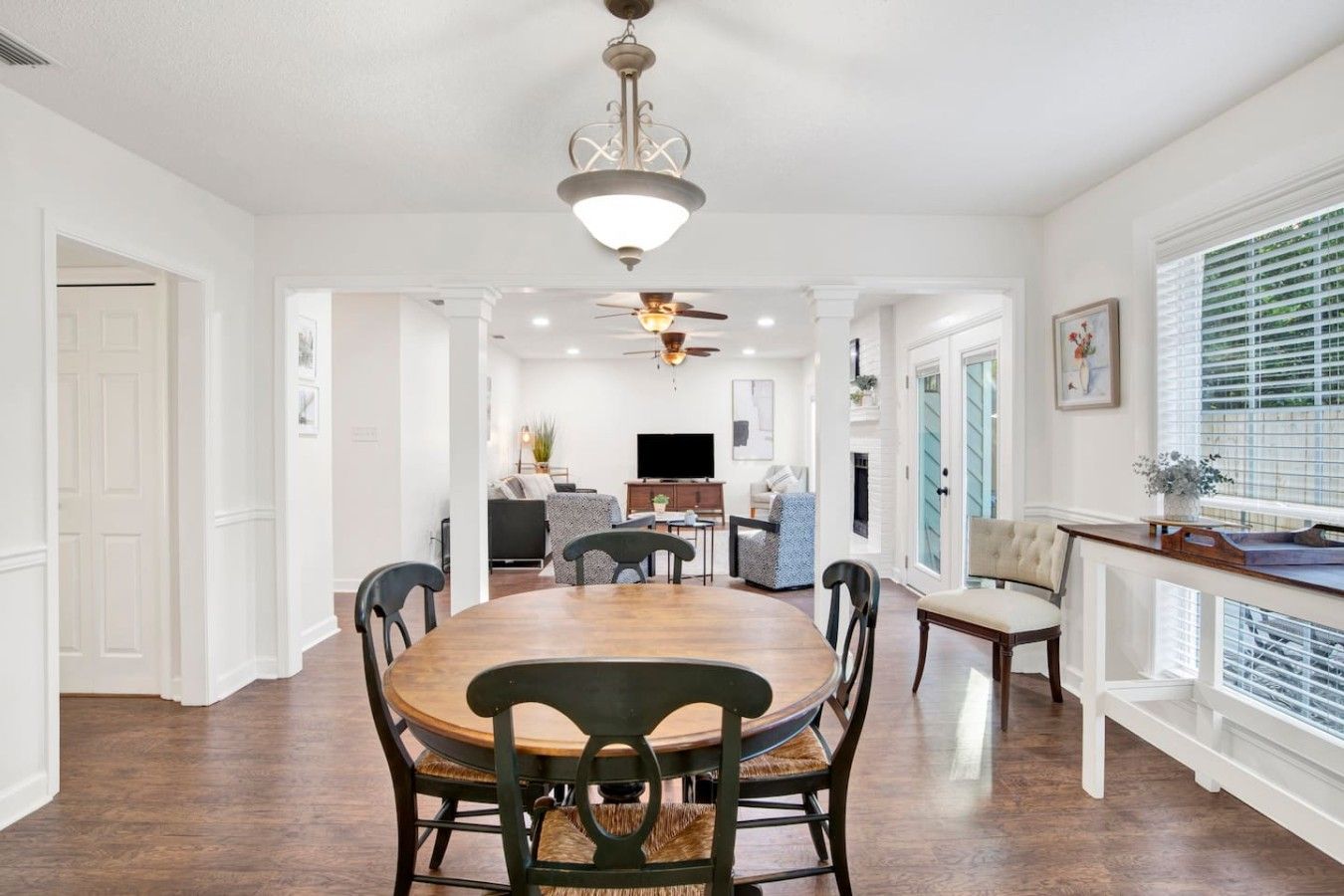 A spacious dining area with a large wooden table and chairs, a ceiling fan, and a view of the living room through an open doorway.