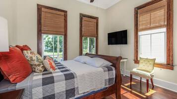 A bedroom with a bed, a chair, a television, and windows with blinds.