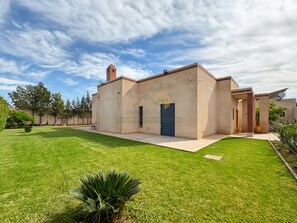 A single-story building with a flat roof, a small tower-like structure on the left, and a blue garage door. - Propriété d’exception à Samanah Golf (marrakech)