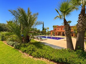 A pool area with lounge chairs, palm trees, and a building with a red facade. - Propriété d’exception à Samanah Golf (marrakech)