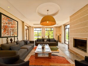 A spacious living room with a fireplace, large windows, and a modern chandelier. - Propriété d’exception à Samanah Golf (marrakech)