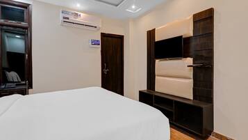 Une chambre d’hôtel comprenant un lit, un téléviseur à écran plat fixé sur un panneau en bois foncé, un climatiseur mural et une porte dotée d’une poignée.