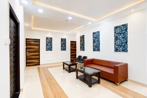 A modern interior with a brown leather sofa, two black chairs, a glass-top coffee table, and a wooden door with a number plate.