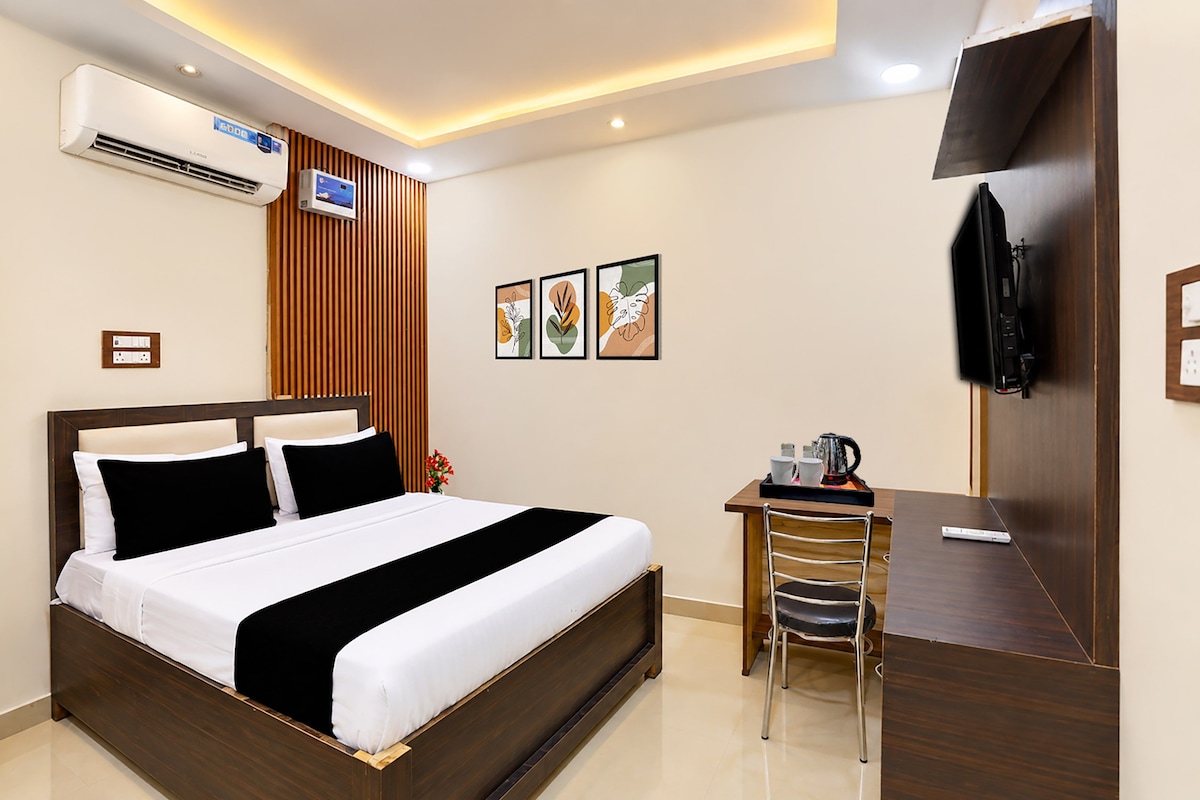 A hotel room with a bed, a desk, a chair, a TV, and artwork on the wall.