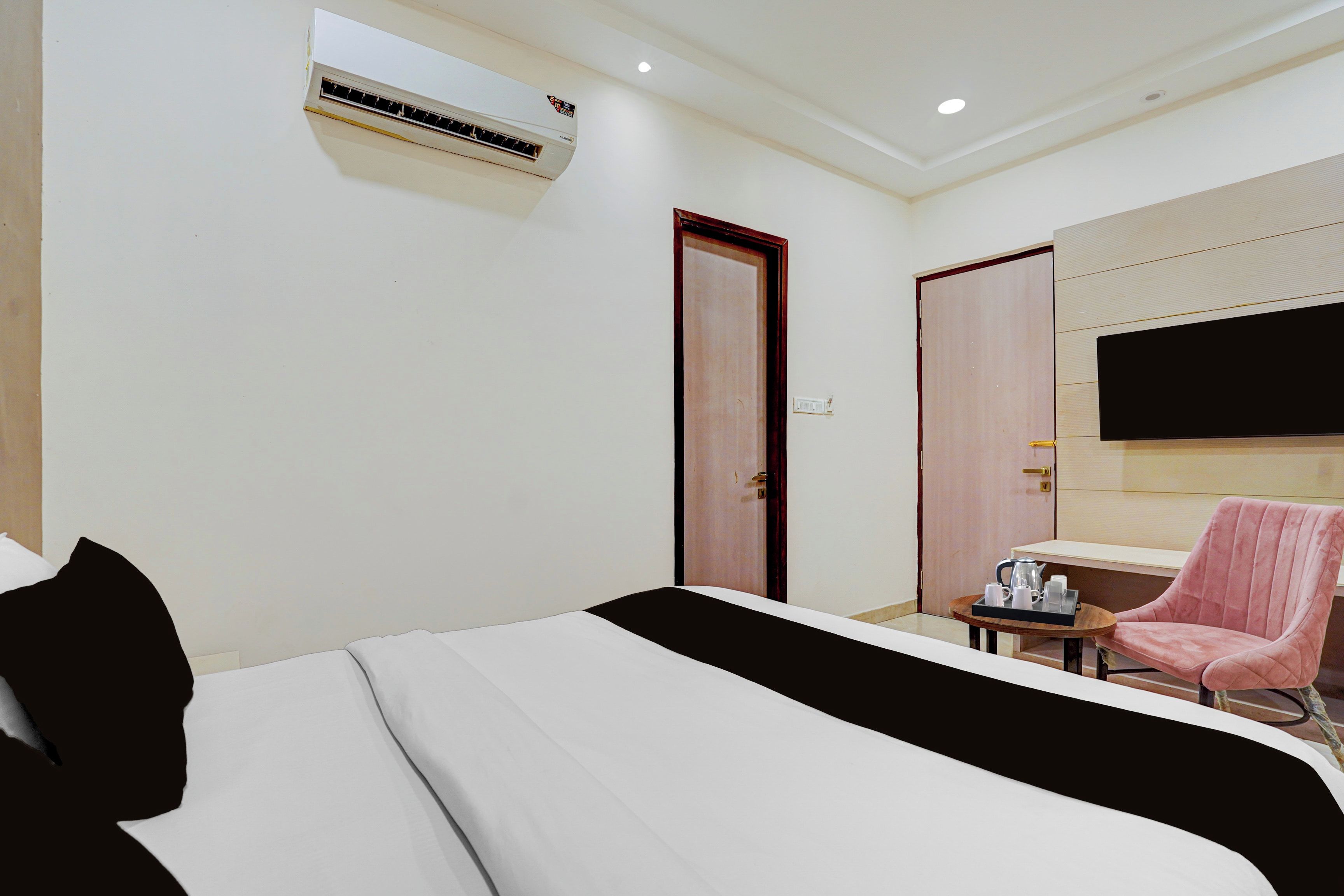 Habitación de hotel con cama, una silla, una mesita con bandeja y televisión montada en la pared.