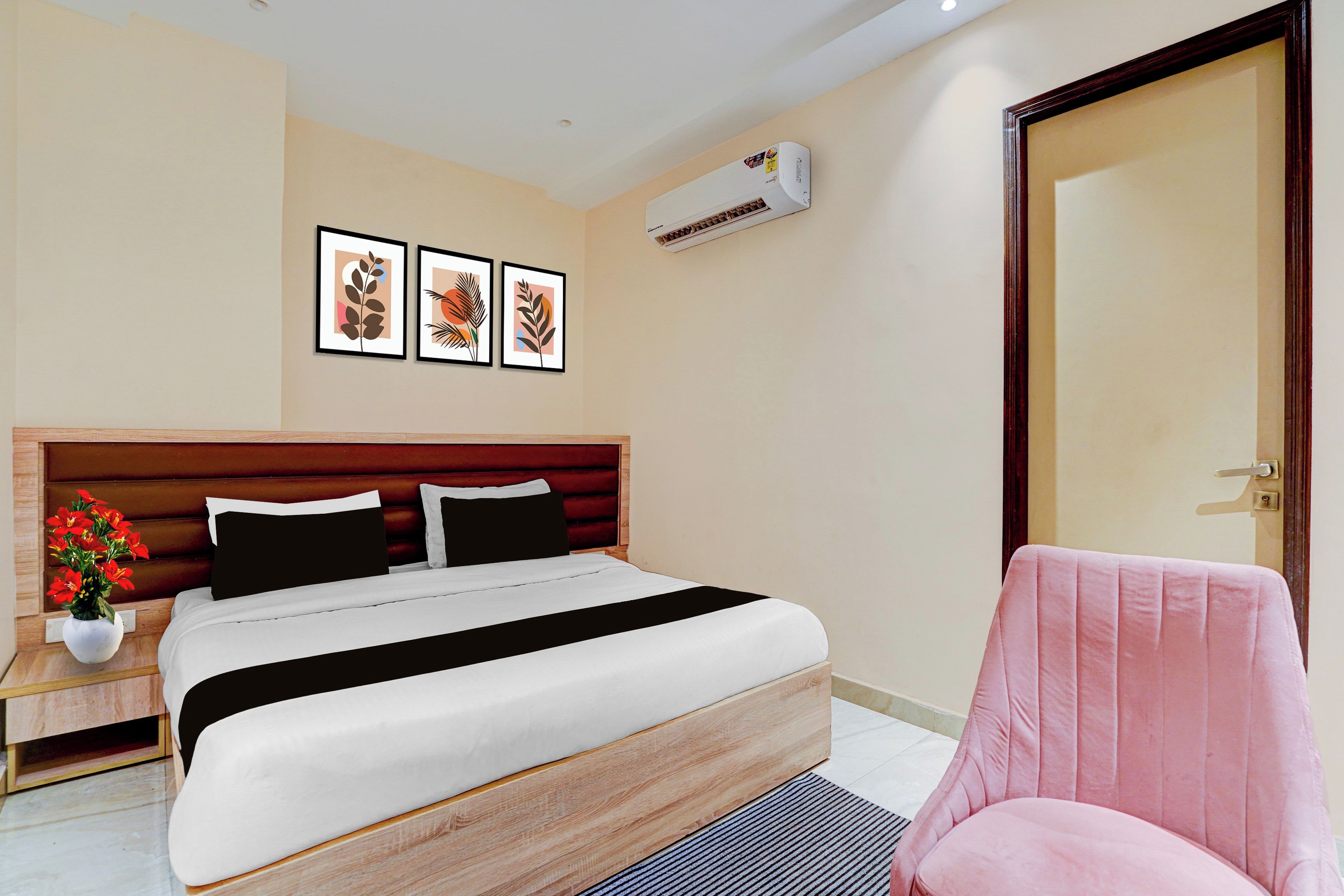 Una camera d'albergo con un letto, una sedia, un comodino, una pianta in vaso e decorazioni alle pareti.